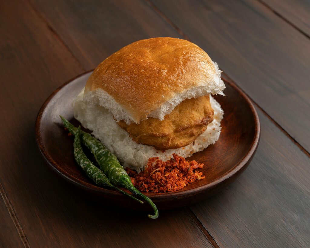 A mouthwatering Vada Pav served with green chili and chutney on a wooden plate.